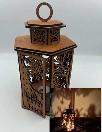 Tall wooden Christmas lantern with intricate winter village cut-outs casting tree-shaped shadows on the wall.