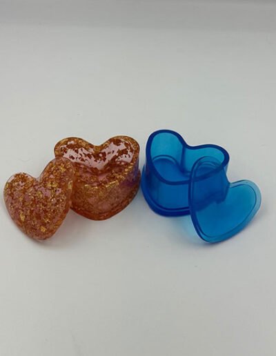 Heart-shaped resin trinket boxes, one in blue and one in gold with flakes, shown with their lids.